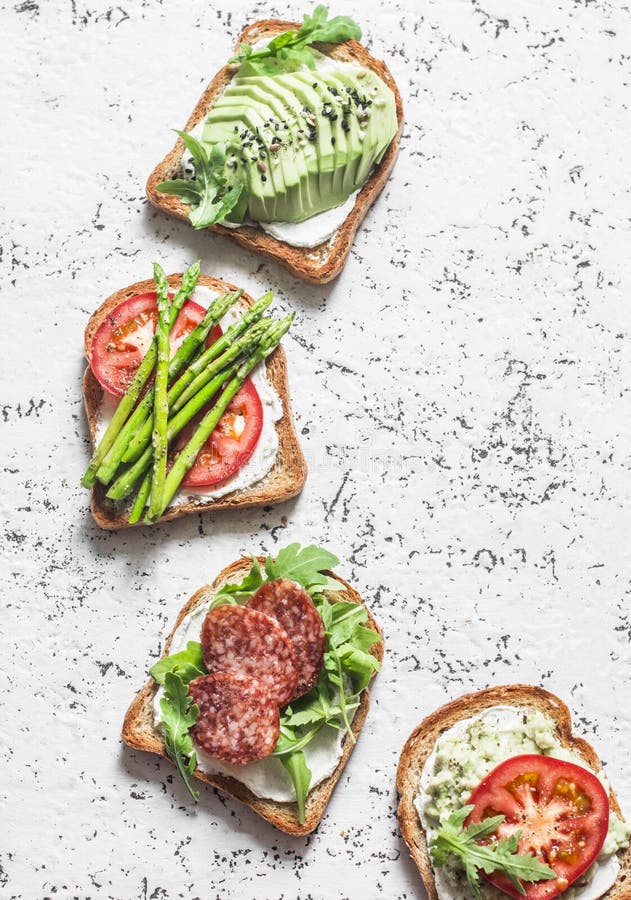 Toast sandwiches with avocado, salami, asparagus, tomatoes and soft cheese on light background, top view. Tasty breakfast, snack o royalty free stock photo