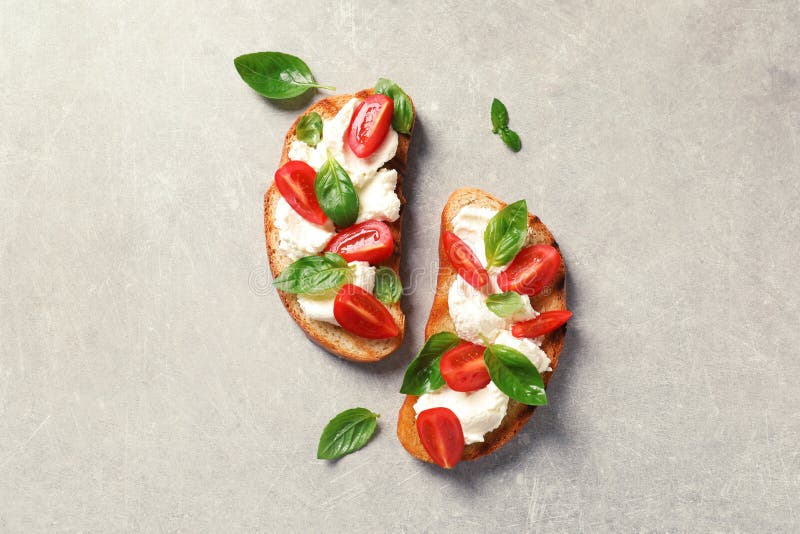Toasted bread with tasty cream cheese and tomatoes on gray background