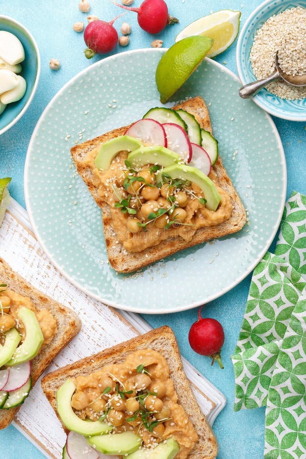 Toasts with chickpea hummus, avocado, fresh radish, cucumber, sesame seeds and flaxseed sprouts. Diet breakfast. Delicious and hea stock image Toasts with chickpea hummus, avocado, fresh radish, cucumber, sesame seeds and flaxseed sprouts. Diet breakfast. Delicious and hea stock image