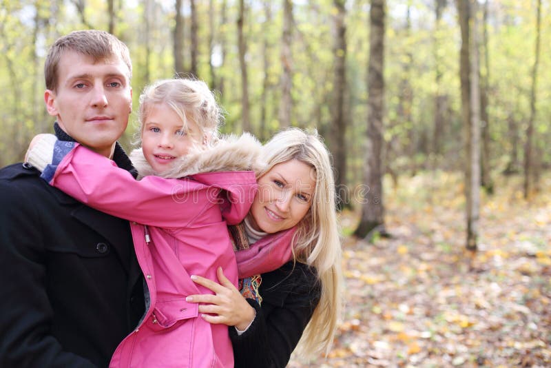 Happy daughter hugs father, and mother peeks out from behind them in autumn forest. Focus on mother. Shallow depth of field. Happy daughter hugs father, and mother peeks out from behind them in autumn forest. Focus on mother. Shallow depth of field.