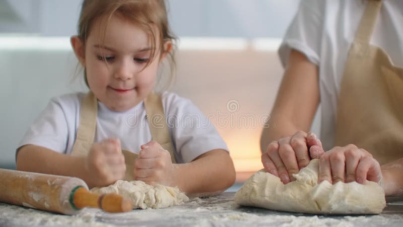 Tochter und Mutter zu Hause in der Küche in den Schutzblechen Gießen Mehl vorsehen, mit einem Nudelholz und modellieren Teig mit stock footage
