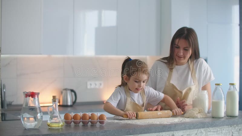 Tochter und Mutter zu Hause in der Küche in den Schutzblechen Gießen Mehl vorsehen, mit einem Nudelholz und modellieren Teig mit stock footage