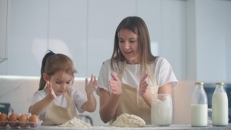 Tochter und Mutter zu Hause in der Küche in den Schutzblechen Gießen Mehl vorsehen, mit einem Nudelholz und modellieren Teig mit stock video