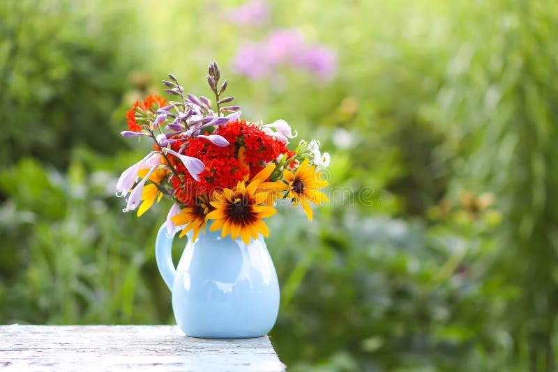 Todavía la vida con el ramo de jardín florece en un florero azul de la cerámica en la tabla al aire libre imagen de archivo Todavía la vida con el ramo de jardín florece en un florero azul de la cerámica en la tabla al aire libre imagen de archivo