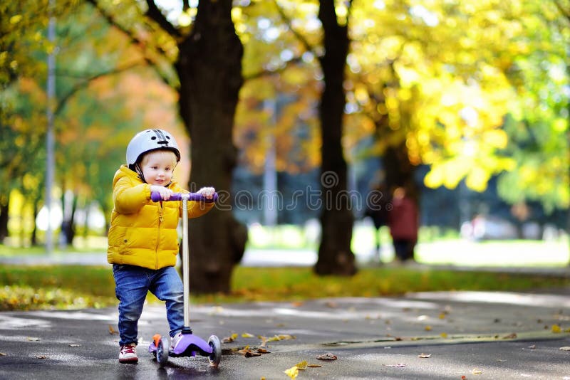 Toddler boy in safety helmet learning to ride scooter