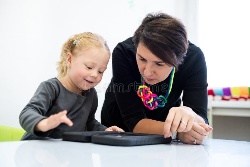 Toddler girl in child occupational therapy session doing playful exercises on a digital tablet with her therapist.