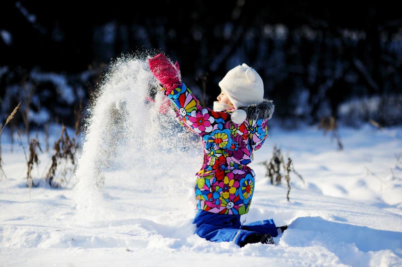 Toddler girl in colorful snowsuit plays in snow