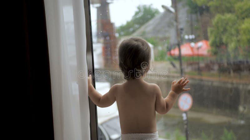 Toddler Wearing Diaper Stands Looking Out Window by Stocksy