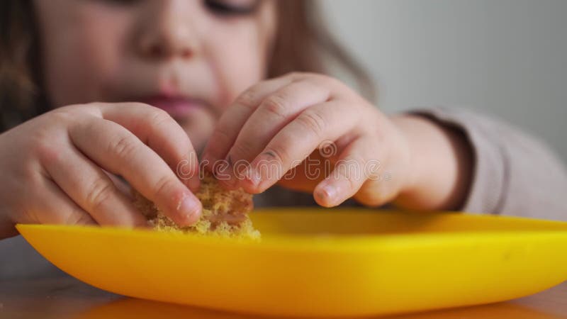 Toddler girl eating bread or pie at home with her hands. Hungry kid. Unhealthy diet. Bad table manners