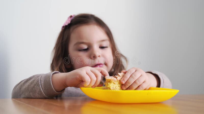 Toddler girl eating bread or pie at home with her hands. Hungry kid. Unhealthy diet. Bad table manners