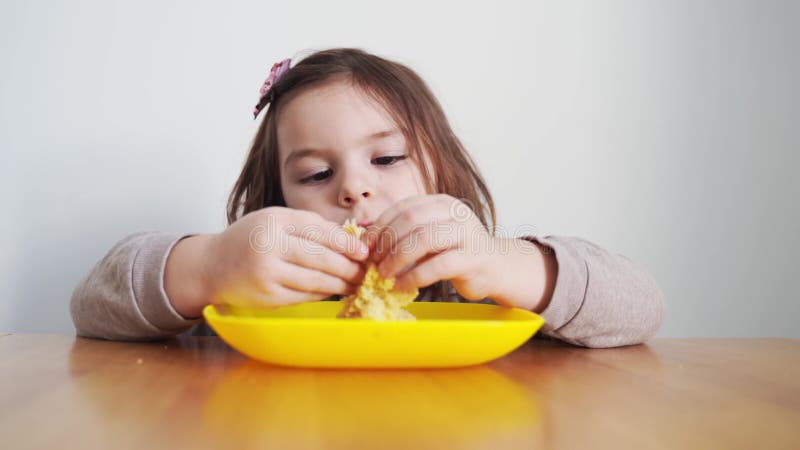 Toddler girl eating bread or pie at home with her hands. Hungry kid. Unhealthy diet. Bad table manners