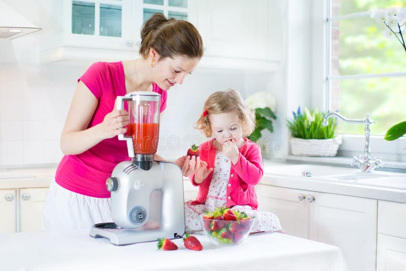 Toddler girl and her mother making fresh strawberry