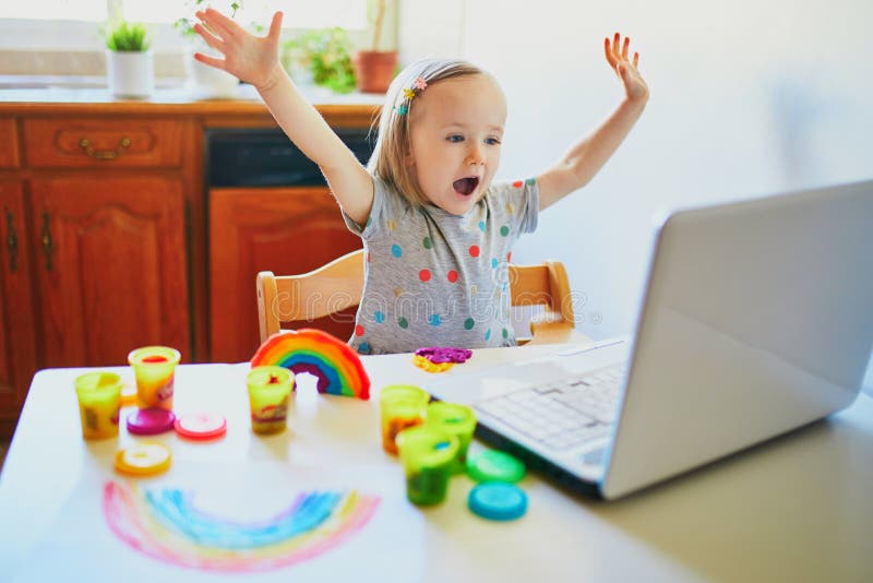 Toddler girl playing modelling clay in front of laptop. Kid using computer to communicate with friends or kindergartners. Education or online communication for