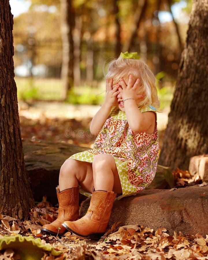 Toddler playing peek-a-boo outside on rock
