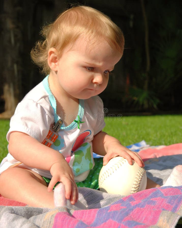 Toddler touching softball and looking at grass