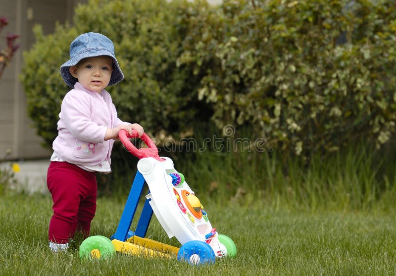 Close up di bambino che indossa cappello floscio spingendo walker giocattolo nel giardino.