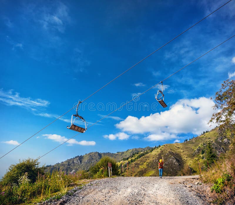 Tourist woman with backpack and yellow pointing to the cableway in the mountain ski resort at summertime. Tourist woman with backpack and yellow pointing to the cableway in the mountain ski resort at summertime