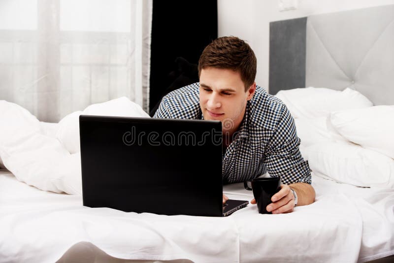 Toevallige jonge mens die laptop in bed thuis met behulp van royalty-vrije stock afbeeldingen Toevallige jonge mens die laptop in bed thuis met behulp van royalty-vrije stock afbeeldingen