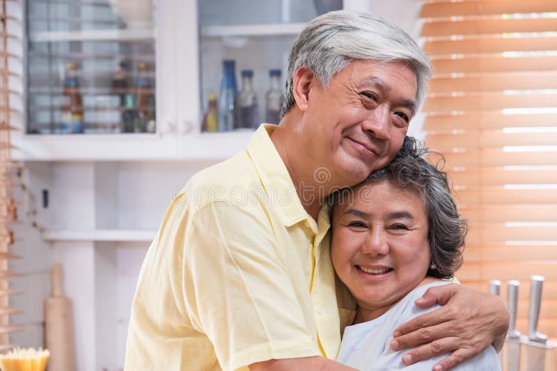 Togerther senior asiatico di abbraccio delle coppie ed esaminare macchina fotografica e sorridere nella cucina a casa concetto fe