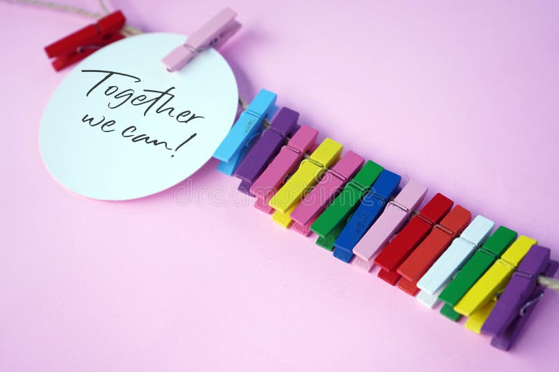 Together we can. Text on white circle paper with colorful paper clips on pink background. Teamwork and togetherness concept.