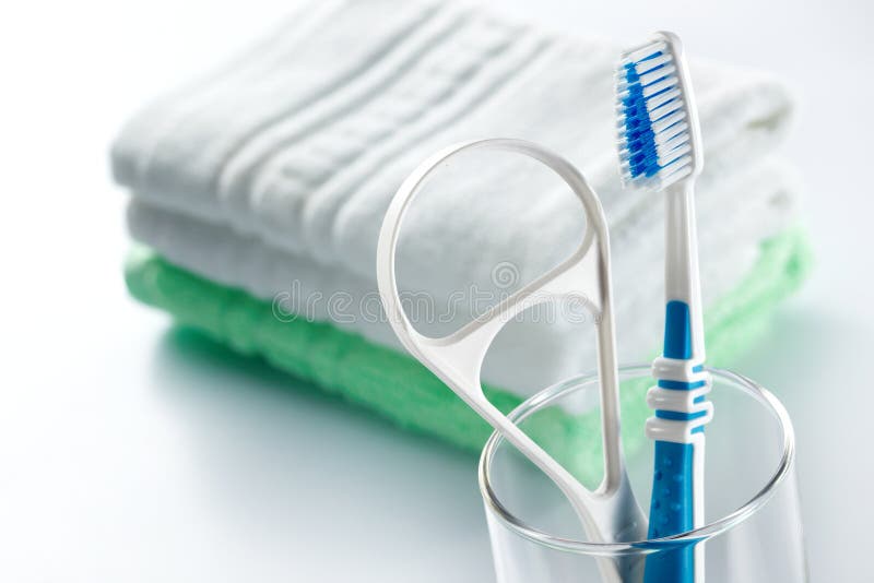 Close-up shot of blue toothbrush and tongue cleaner in a glass accompanied with face towels. Close-up shot of blue toothbrush and tongue cleaner in a glass accompanied with face towels