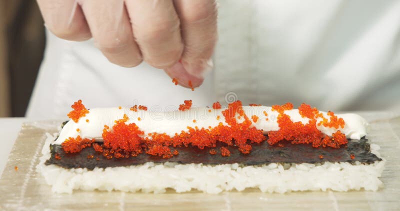 Toma de conciencia de las manos del chef en guantes preparando sushi deliciosos rollitos con queso suave y tobiko en la cocina almacen de video