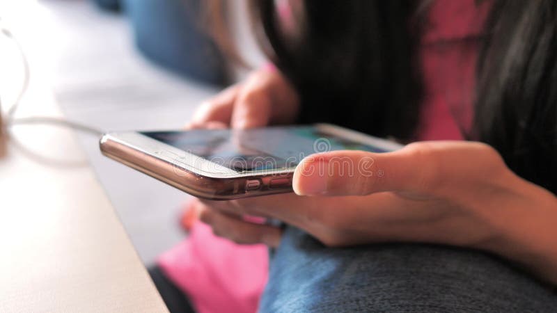 Toma de las manos de una joven mujer escribiendo algo en la pantalla táctil de un teléfono inteligente en la sala de estar