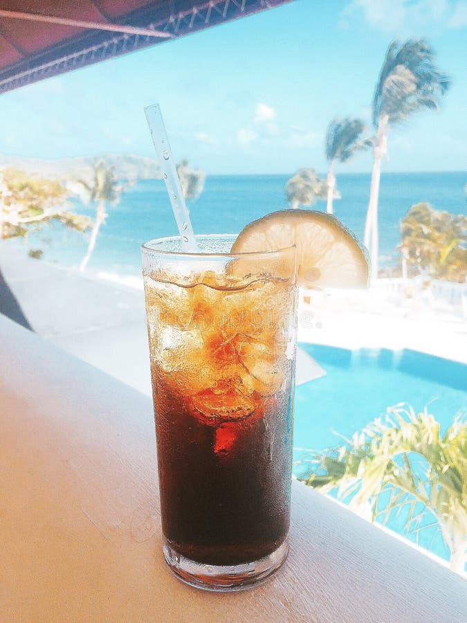 Toma vertical de un vaso de coque frío con limón sobre una mesa de bar cerca de la playa imagen de archivo libre de regalías