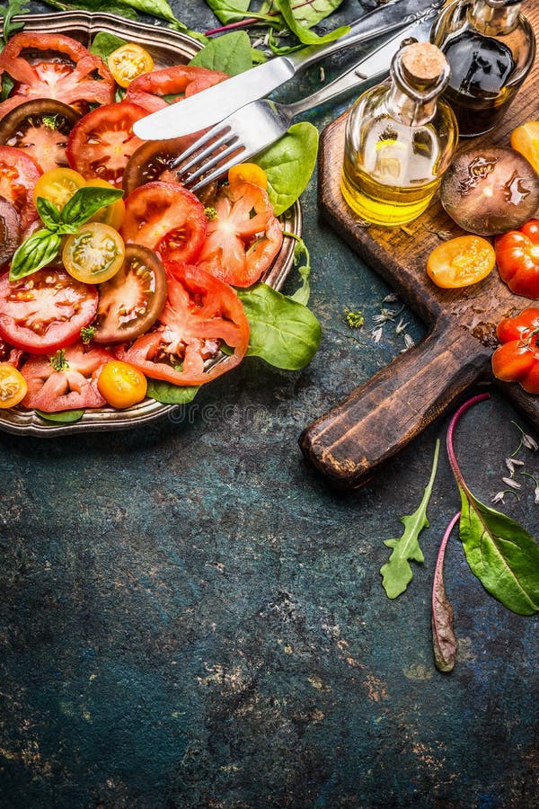 Tomate cu diferite tomate colorate ulei de măsline și oțet balsamat. placă cu tomate, tacâmuri și ingrediente pentru salată stock image