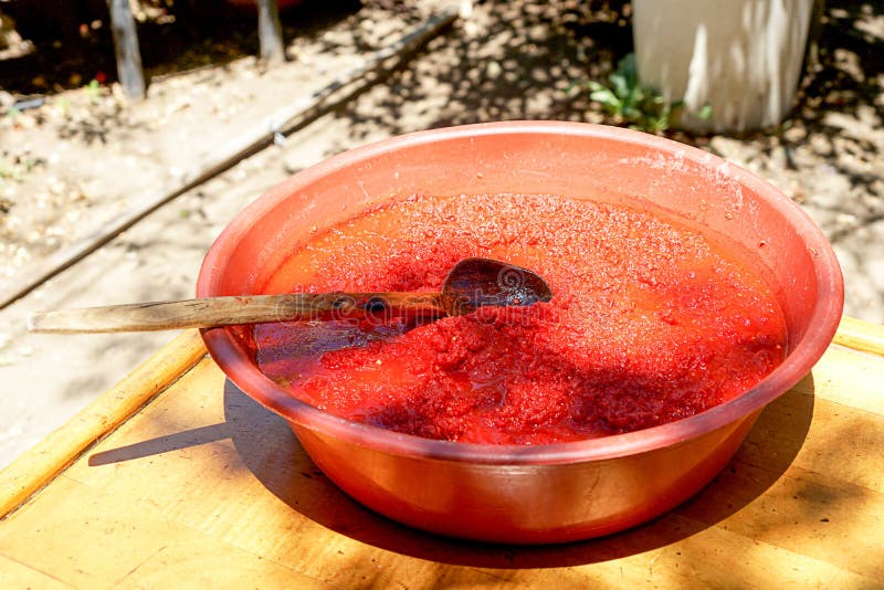 Tomate de mezcla revuelto con la cuchara de madera. La pasta de tomate recién preparada refleja la luz en superficie y que es suscitada con la cuchara de madera