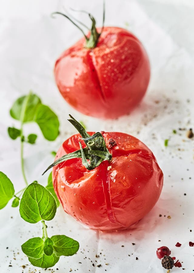 Tomate entero asado o asado a la parrilla con el condimento. Tomate entero asado o asado a la parrilla fresco con el condimento y albahaca fresca en el Libro Blanco arrugado en un cierre encima de la visión