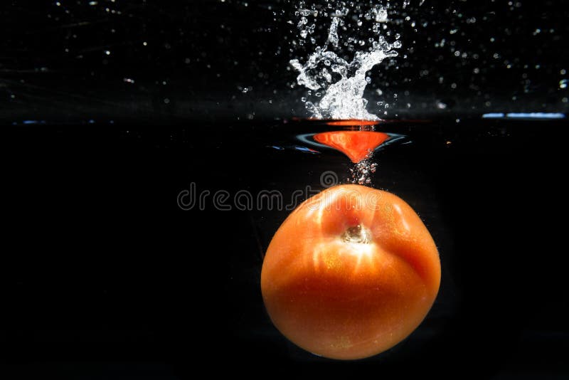 Tomate que cai na água e que espirra gotas no backg preto imagens de stock royalty free Tomate que cai na água e que espirra gotas no backg preto imagens de stock royalty free