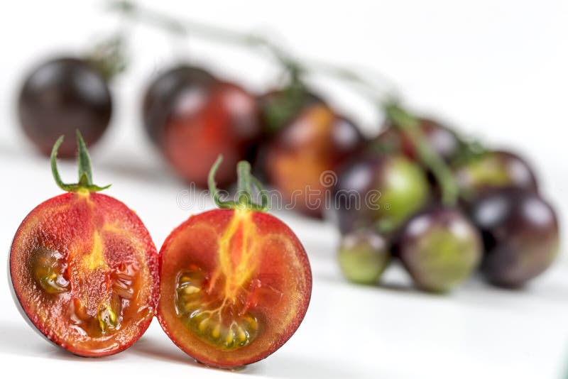 Tomate Yoom en macro tranch e en deux. Tomato Yoom sliced in front of the entire bunch on a white background.