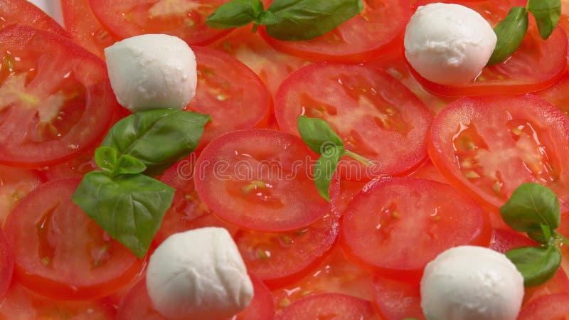 Tomates frescos en rodajas con hojas de albahaca frescas y bolas de mozzarella para el carpaccio de tomate rotar como fondo almacen de metraje de vídeo