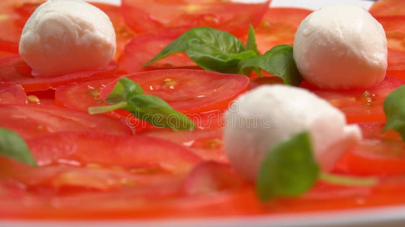 Tomates frescos en rodajas con hojas de albahaca frescas y bolas de mozzarella para el carpaccio de tomate rotar como fondo metrajes