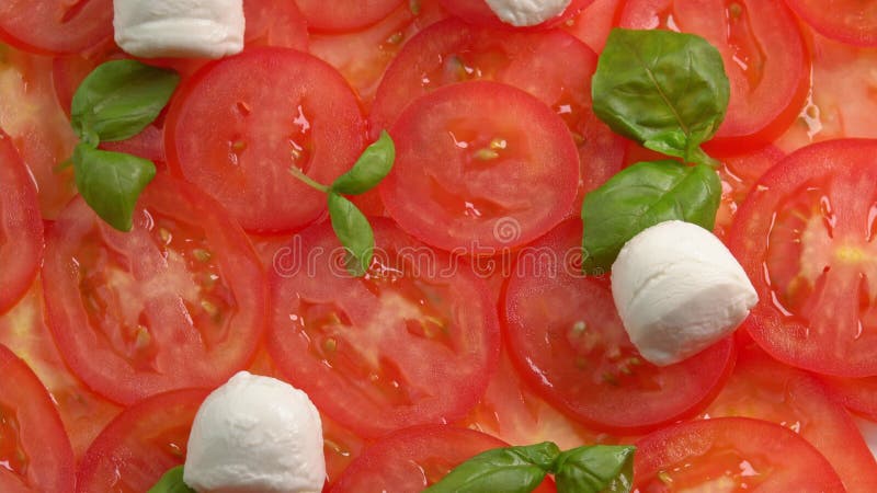 Tomates frescos en rodajas con hojas de albahaca frescas y bolas de mozzarella para el carpaccio de tomate rotar como fondo almacen de metraje de vídeo