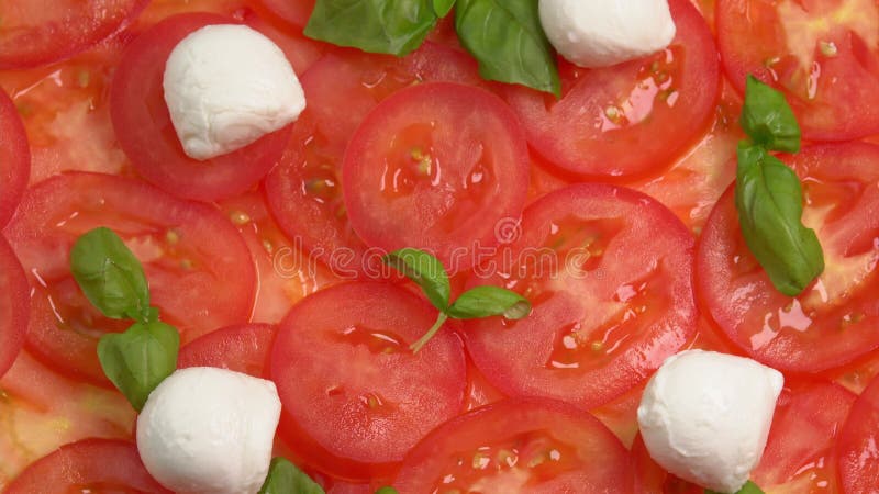 Tomates frescos en rodajas con hojas de albahaca frescas y bolas de mozzarella para el carpaccio de tomate rotar como fondo almacen de video