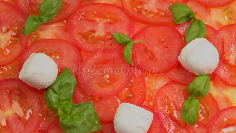 Tomates frescos en rodajas con hojas de albahaca frescas y bolas de mozzarella para el carpaccio de tomate rotar como fondo metrajes