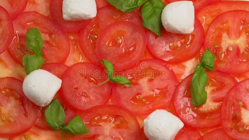 Tomates frescos en rodajas con hojas de albahaca frescas y bolas de mozzarella para el carpaccio de tomate rotar como fondo almacen de video