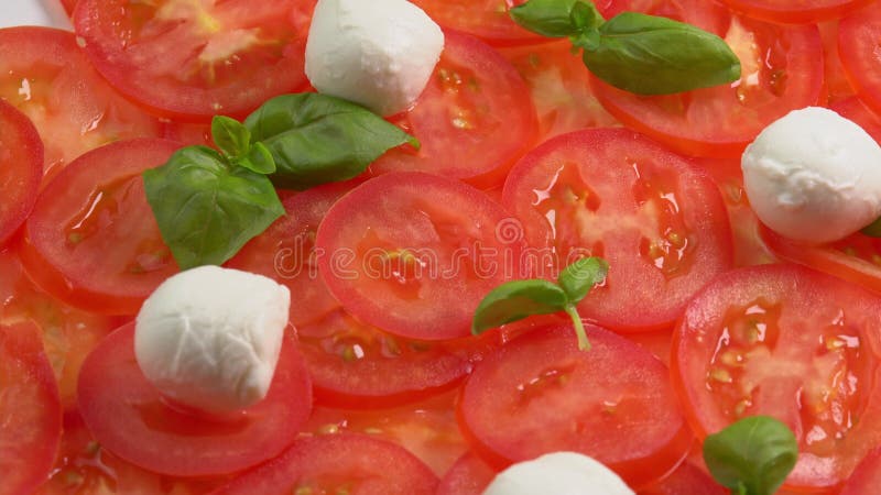 Tomates frescos en rodajas con hojas de albahaca frescas y bolas de mozzarella para el carpaccio de tomate rotar como fondo almacen de metraje de vídeo