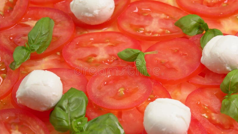 Tomates frescos en rodajas con hojas de albahaca frescas y bolas de mozzarella para el carpaccio de tomate rotar como fondo almacen de video