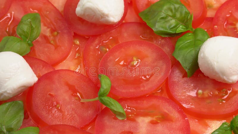 Tomates frescos en rodajas con hojas de albahaca frescas y bolas de mozzarella para el carpaccio de tomate rotar como fondo almacen de video