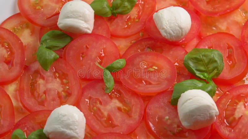 Tomates frescos en rodajas con hojas de albahaca frescas y bolas de mozzarella para el carpaccio de tomate rotar como fondo almacen de video