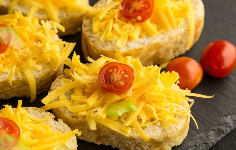 Tomates rallados del queso cheddar y de cereza en rebanadas de baguette fotos de archivo libres de regalías Tomates rallados del queso cheddar y de cereza en rebanadas de baguette fotos de archivo libres de regalías