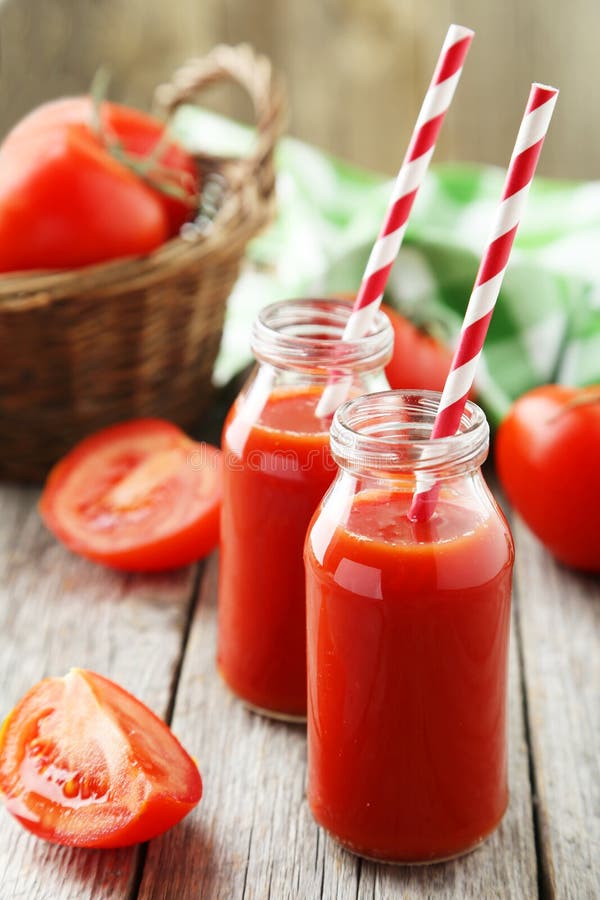 Tomates vermelhos frescos na cesta e suco em umas garrafas no fundo de madeira cinzento imagens de stock Tomates vermelhos frescos na cesta e suco em umas garrafas no fundo de madeira cinzento imagens de stock