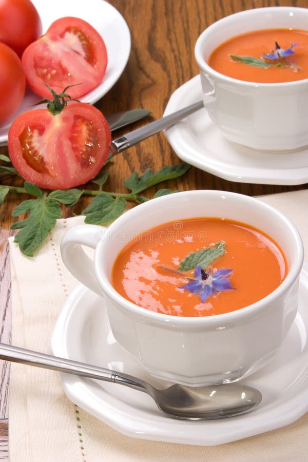 Two bowls of delicious tomato soup garnished with borage flower and leaves. Two bowls of delicious tomato soup garnished with borage flower and leaves