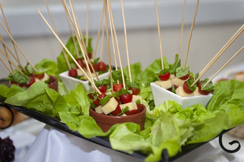 tomatoes cheese basil skewer in bowls on tray decorated with lettuce leaves on event table. tomatoes cheese basil skewer in bowls on tray decorated with lettuce leaves on event table