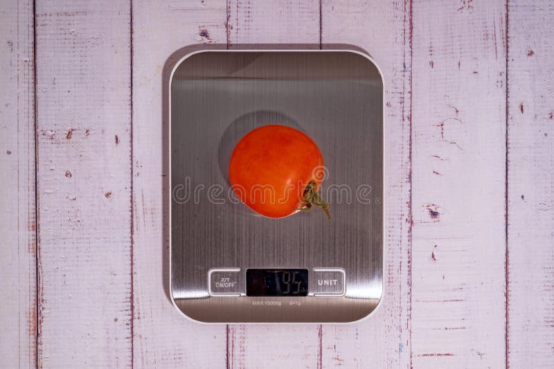 An Tomato Lies on a Digital Kitchen Scale on a Table of Light Boards