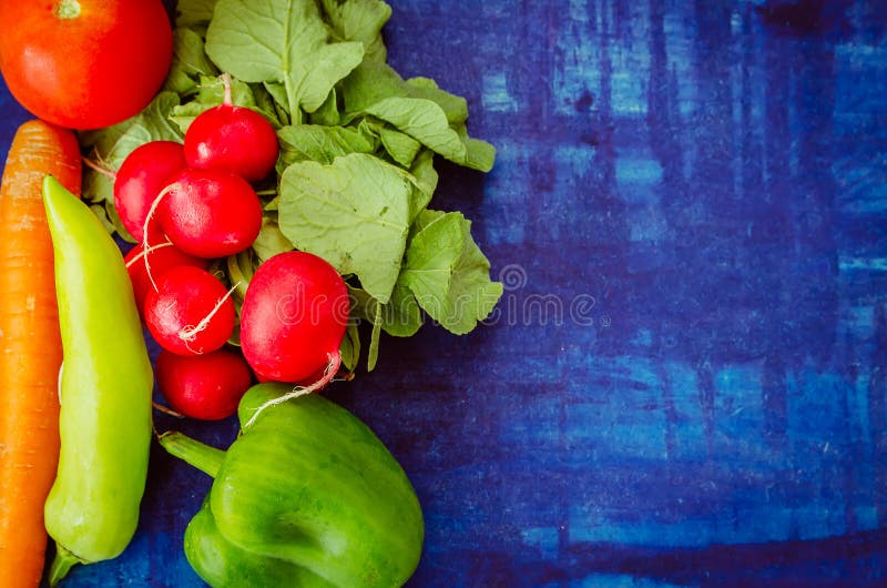 Tomato with radish, cucumber, capsicum and carrot on blue background. Healthy vegetable food concept.