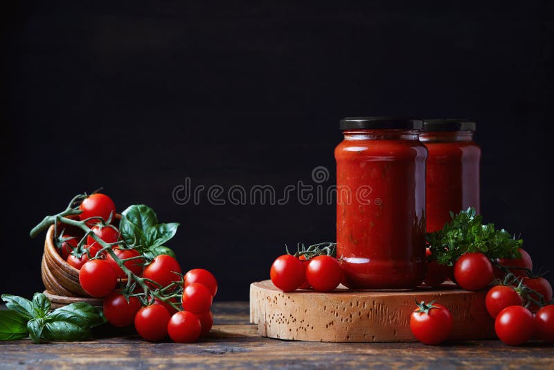 Tomato sauce in a glass jar, tomatoes and herbs on its side.